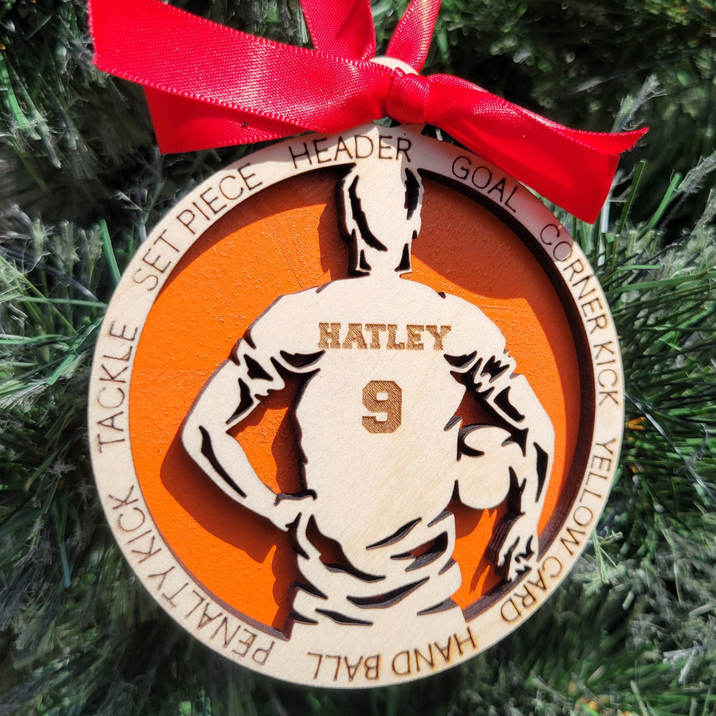Decorative sports-themed ornament with a red ribbon on a Christmas tree. soccer player christmas gift, christmas ornament for soccer player, personalized soccer player christmas ornament