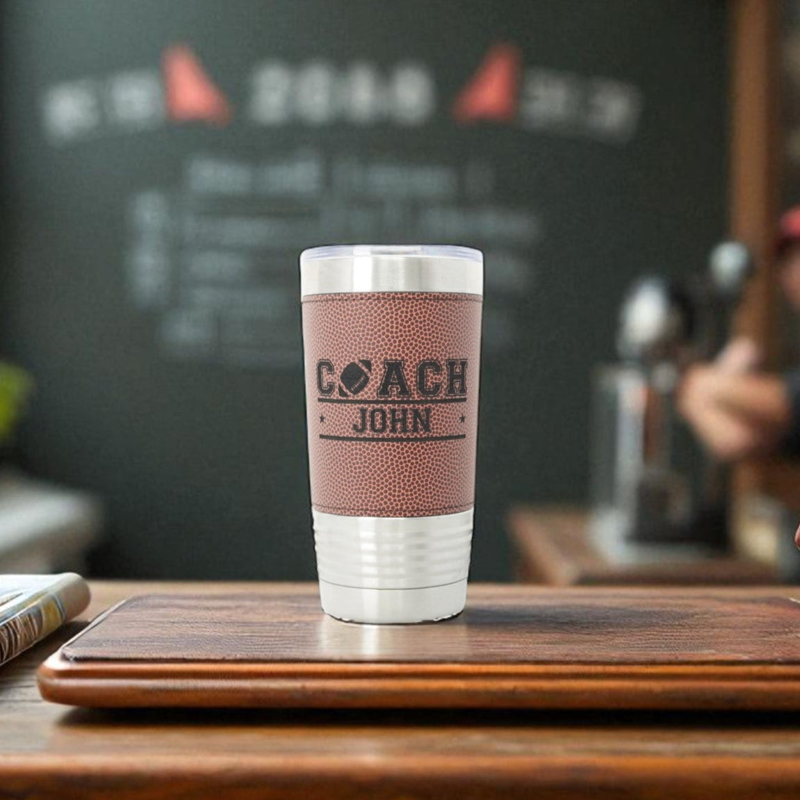 Football-patterned tumbler with 'Coach John' engraving on a wooden surface.