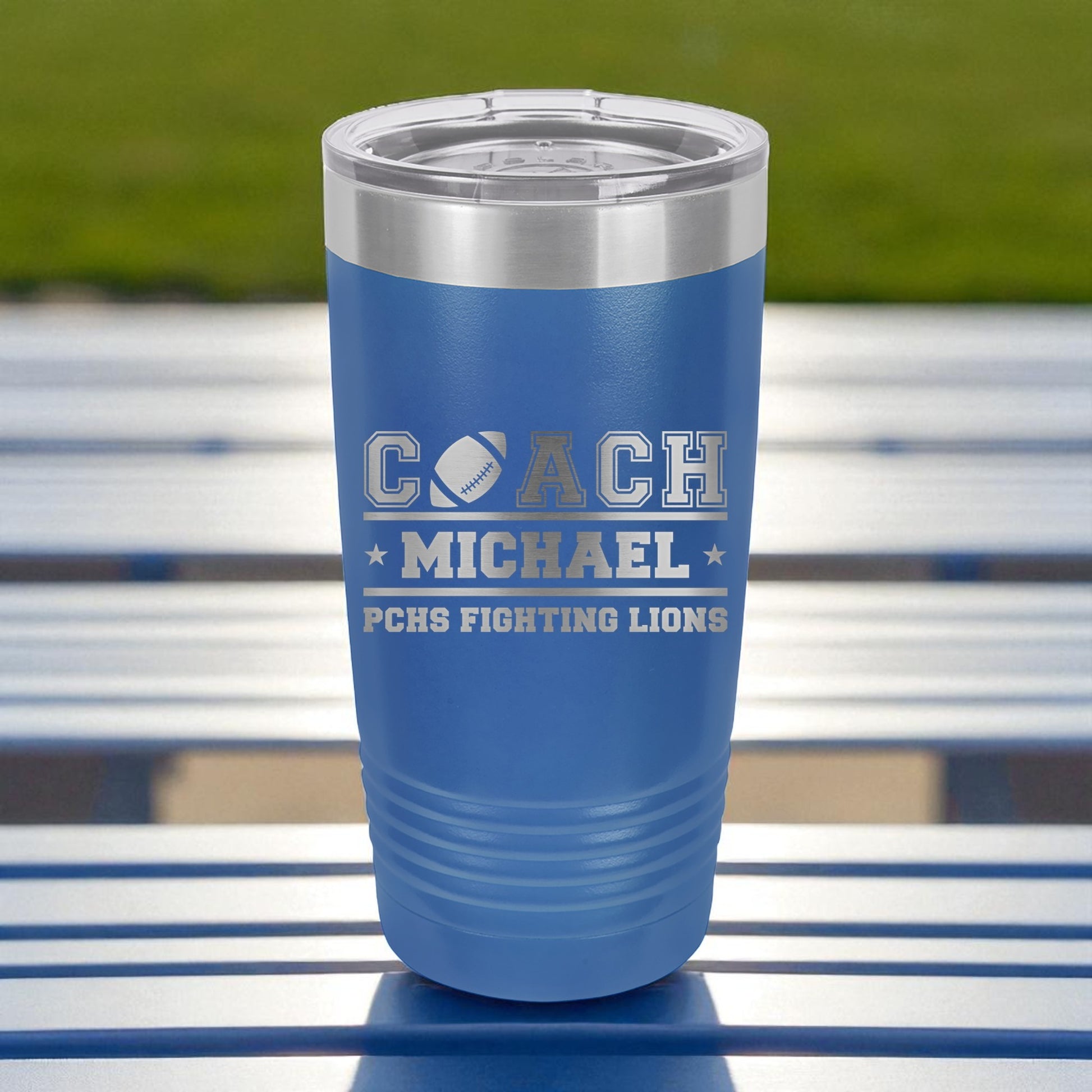 Blue tumbler with 'COACH MICHAEL' and 'PCHS FIGHTING LIONS' text on a metal surface.
