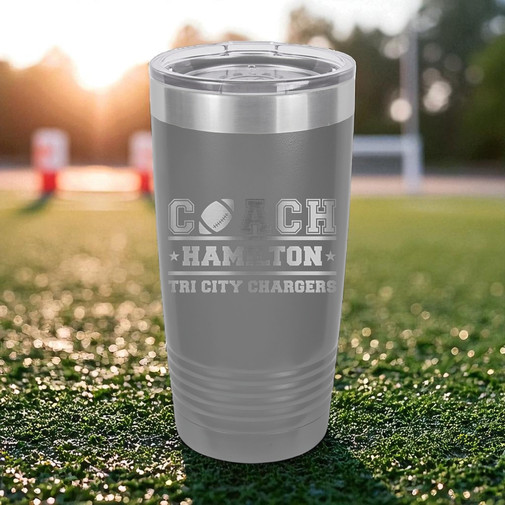 Gray tumbler with 'Coach Hamilton Tri City Chargers' text on a grassy field background