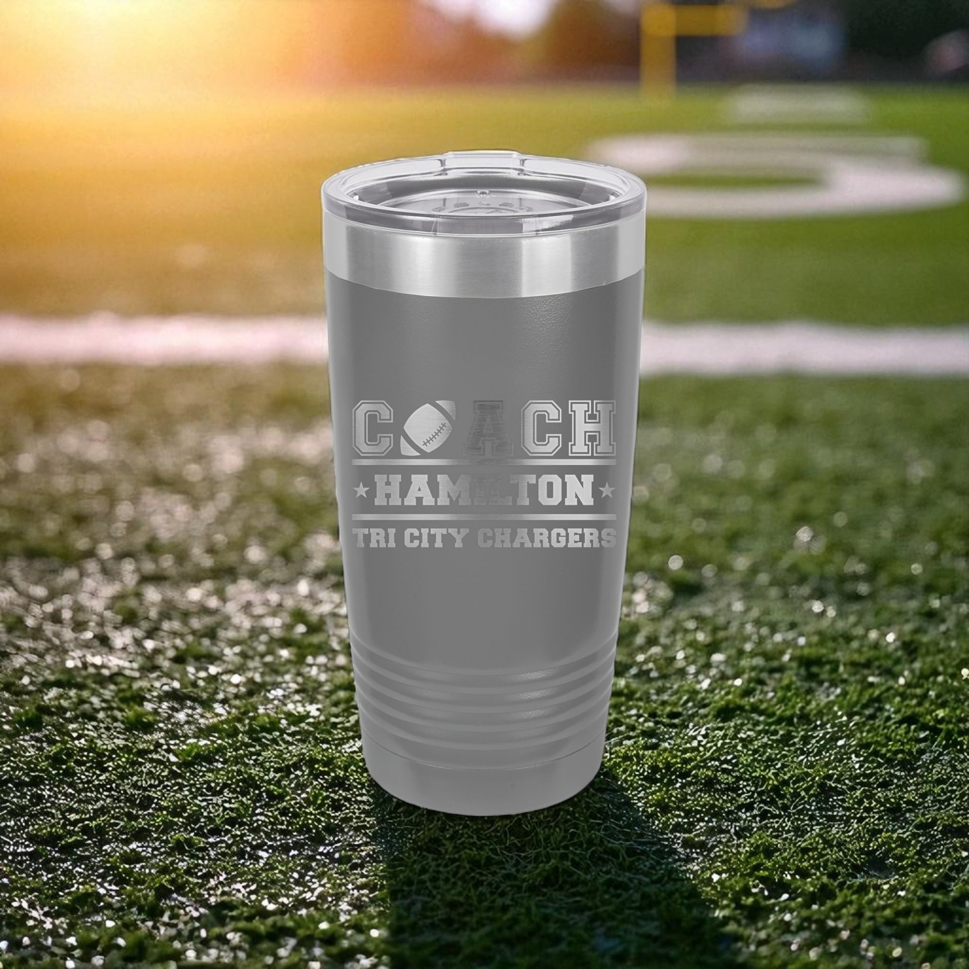 Gray tumbler with engraved text on a grassy field