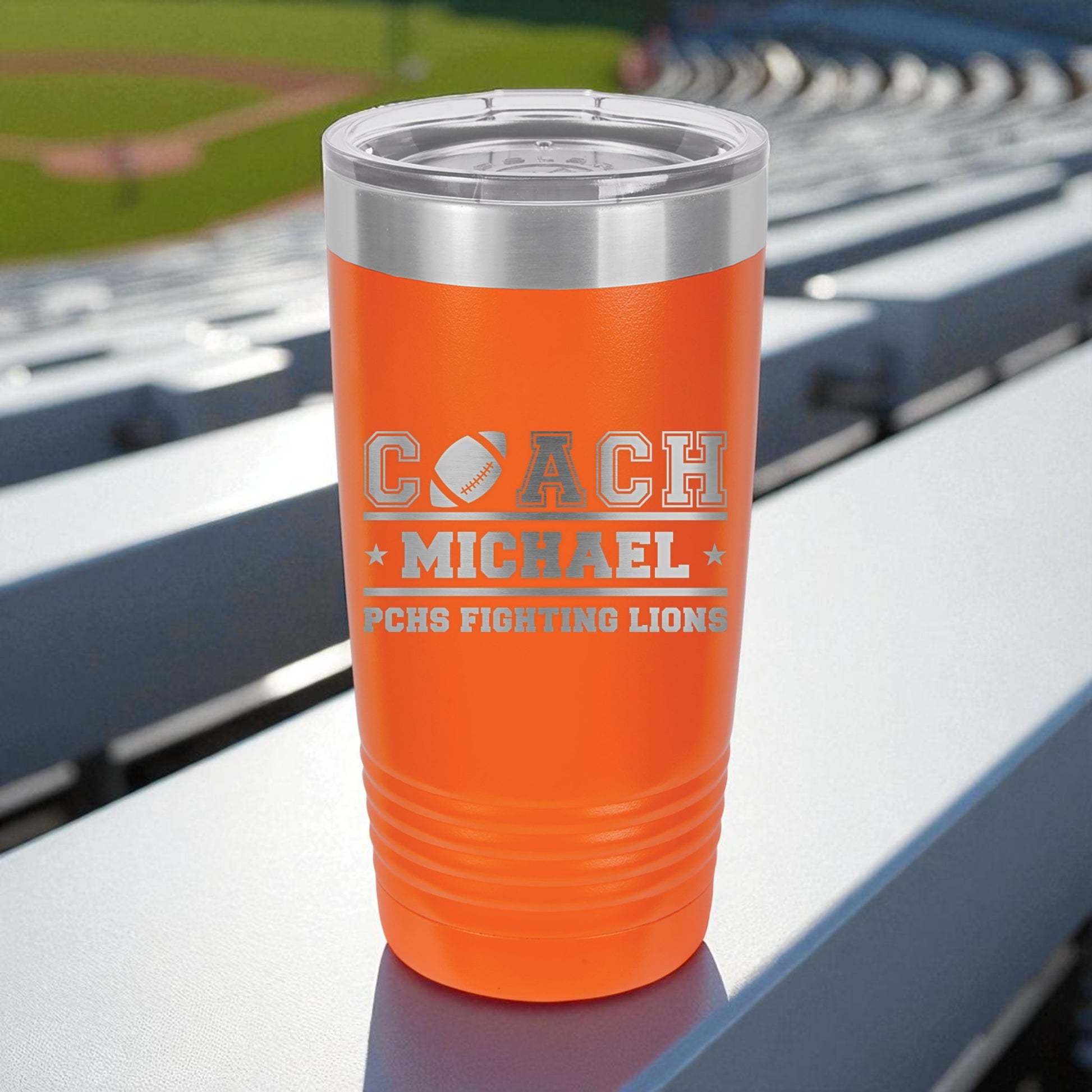 Orange tumbler with engraved text on a stadium bench