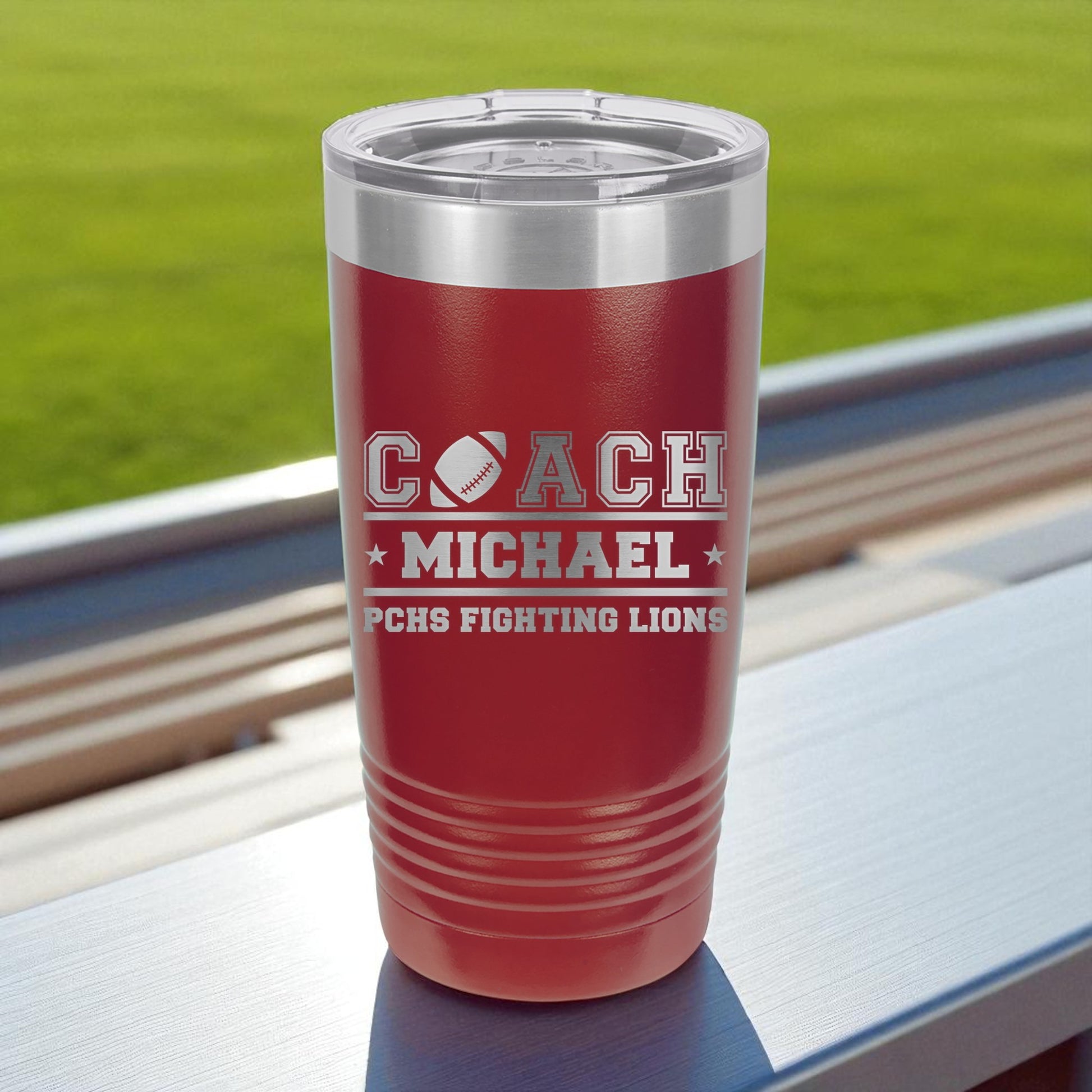 Red insulated tumbler with engraved text on a surface with a grassy background