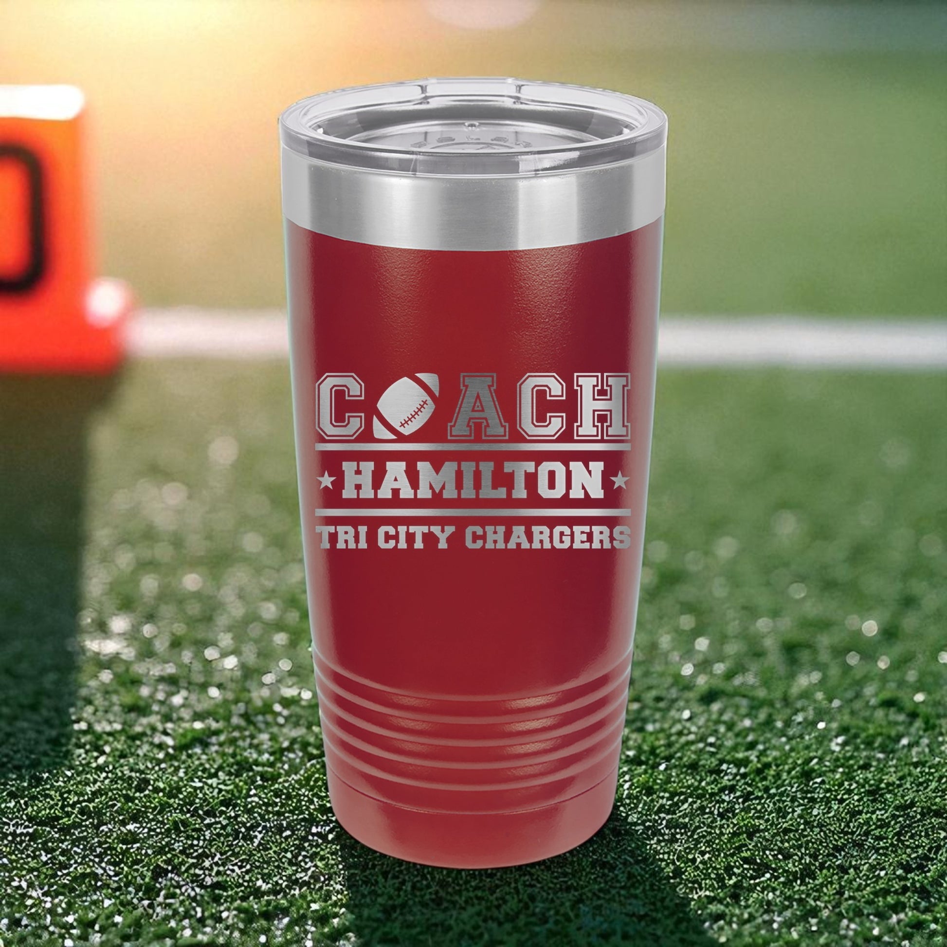 Red tumbler with 'Coach Hamilton Tri City Chargers' text on a grassy field background