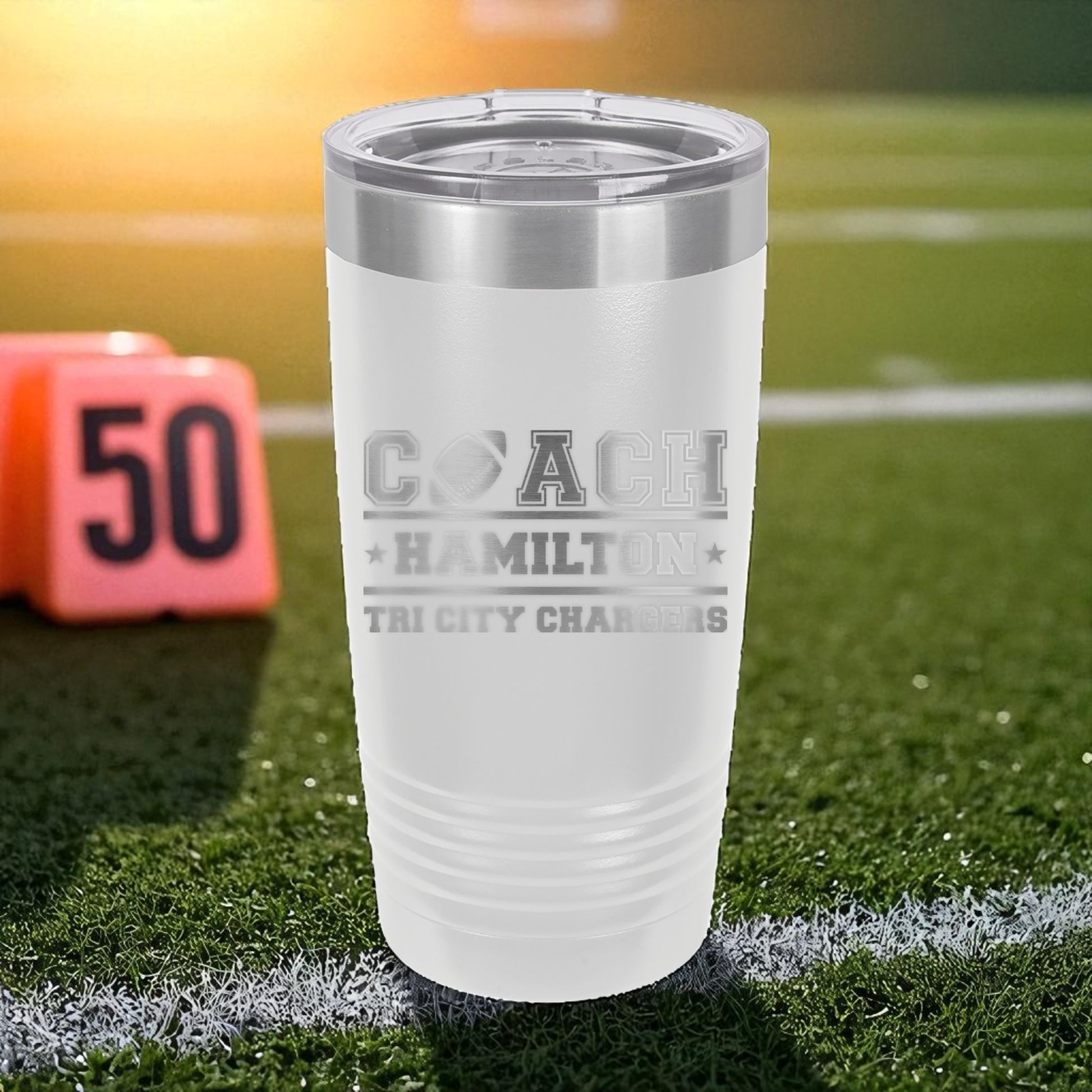 White tumbler with engraved text on a football field