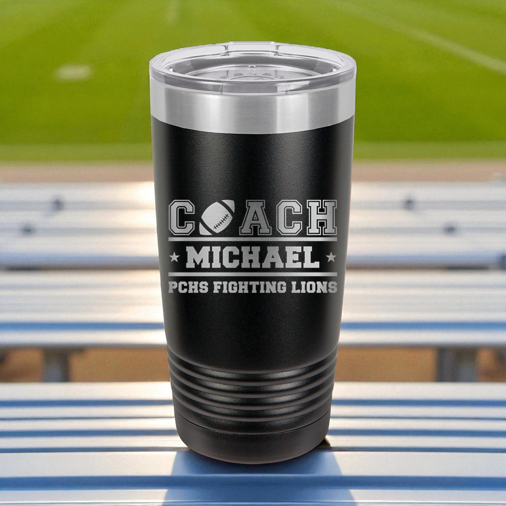 Black insulated tumbler with engraved text on a stadium bench