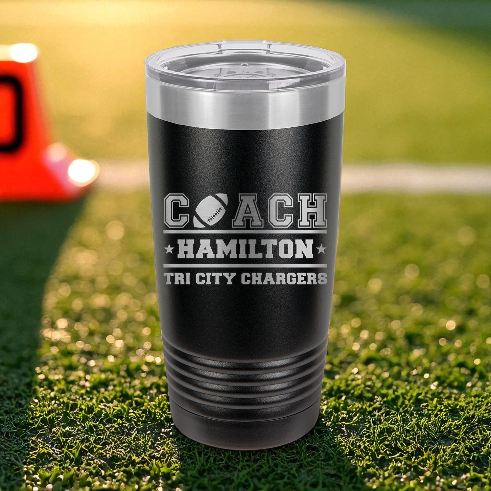 Black tumbler with 'Coach Hamilton Tri City Chargers' text on grass