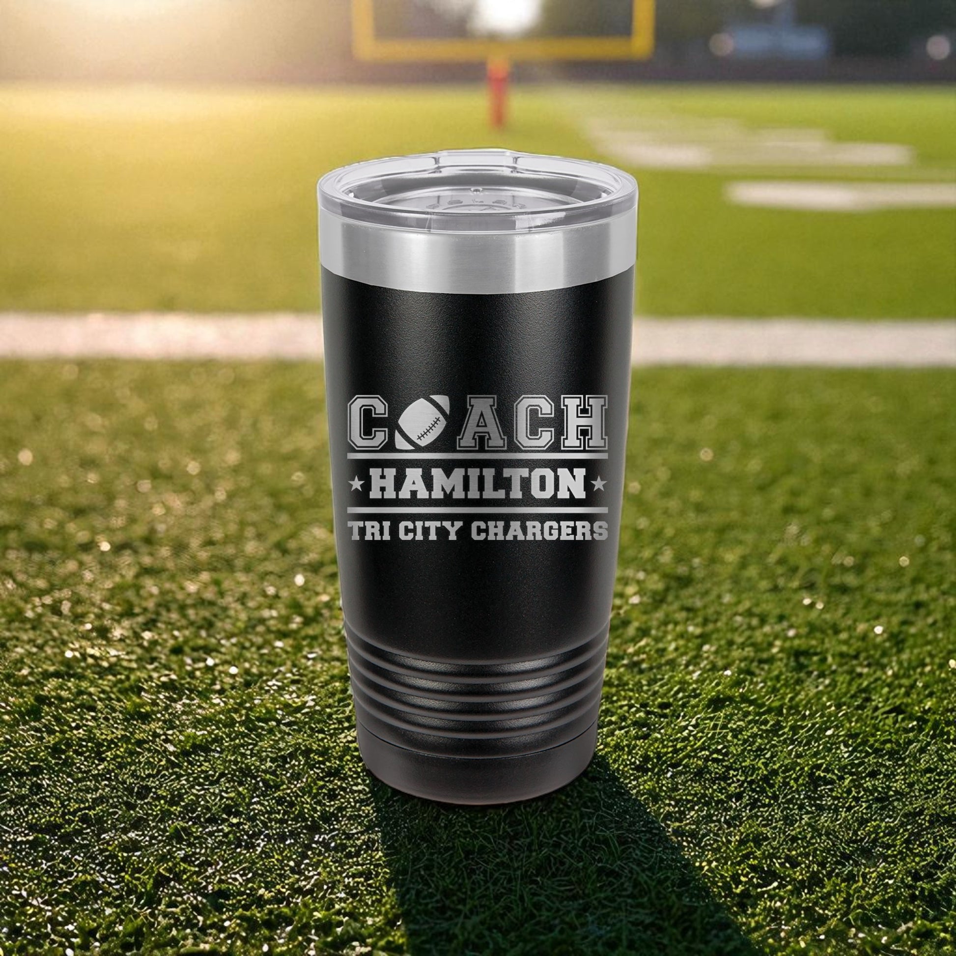 Black tumbler with engraved text on a grassy field background