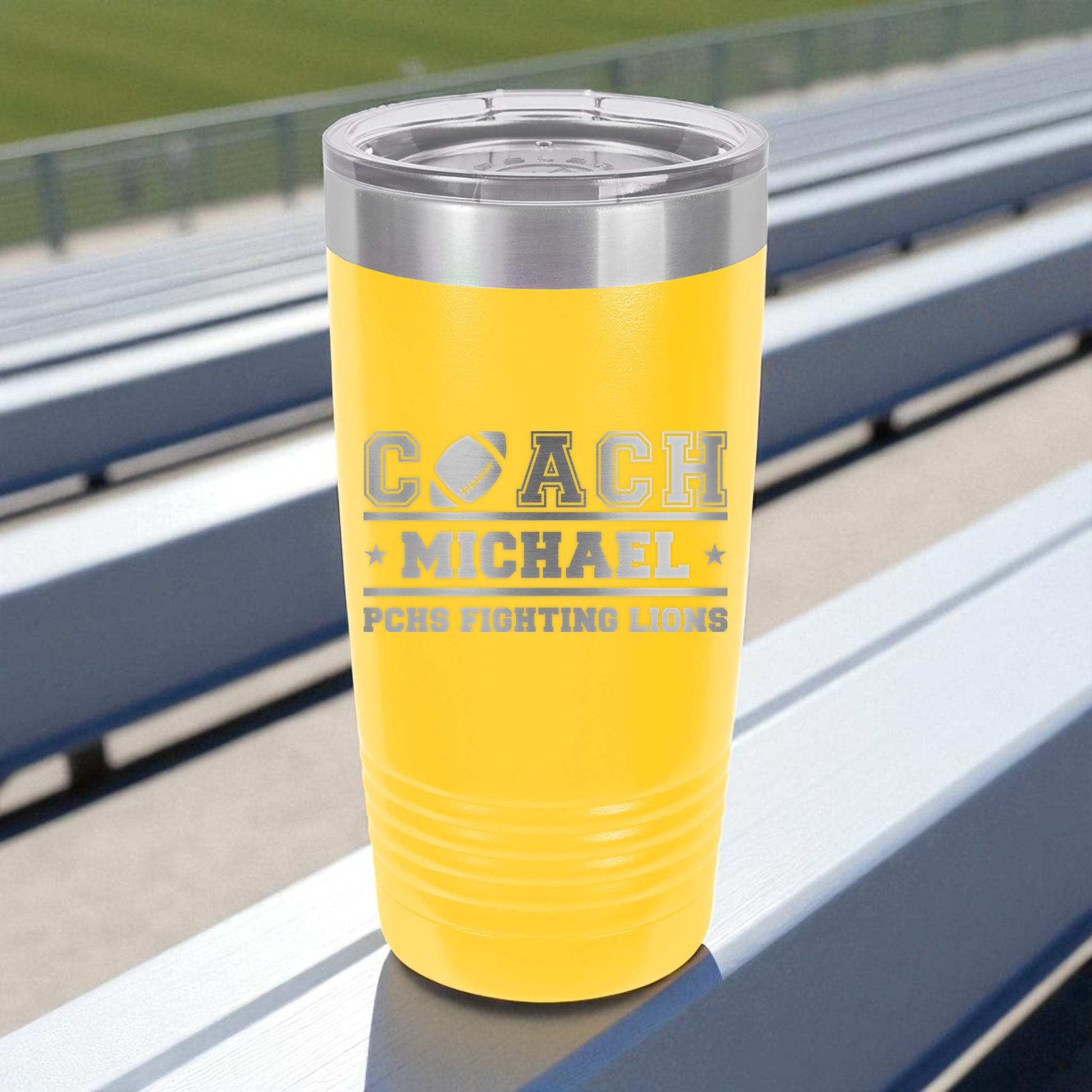 Yellow tumbler with engraved text on a sports stadium bench