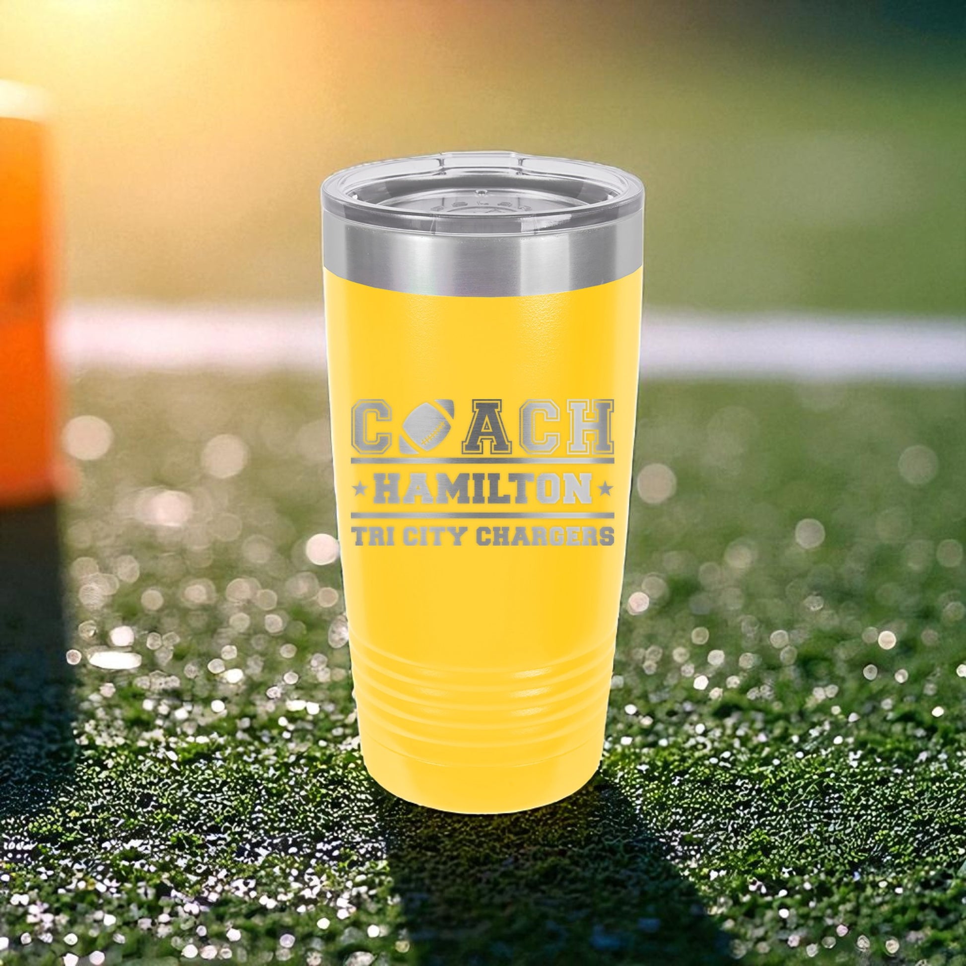 Yellow tumbler with 'COACH HAMILTON' text on a grassy field background