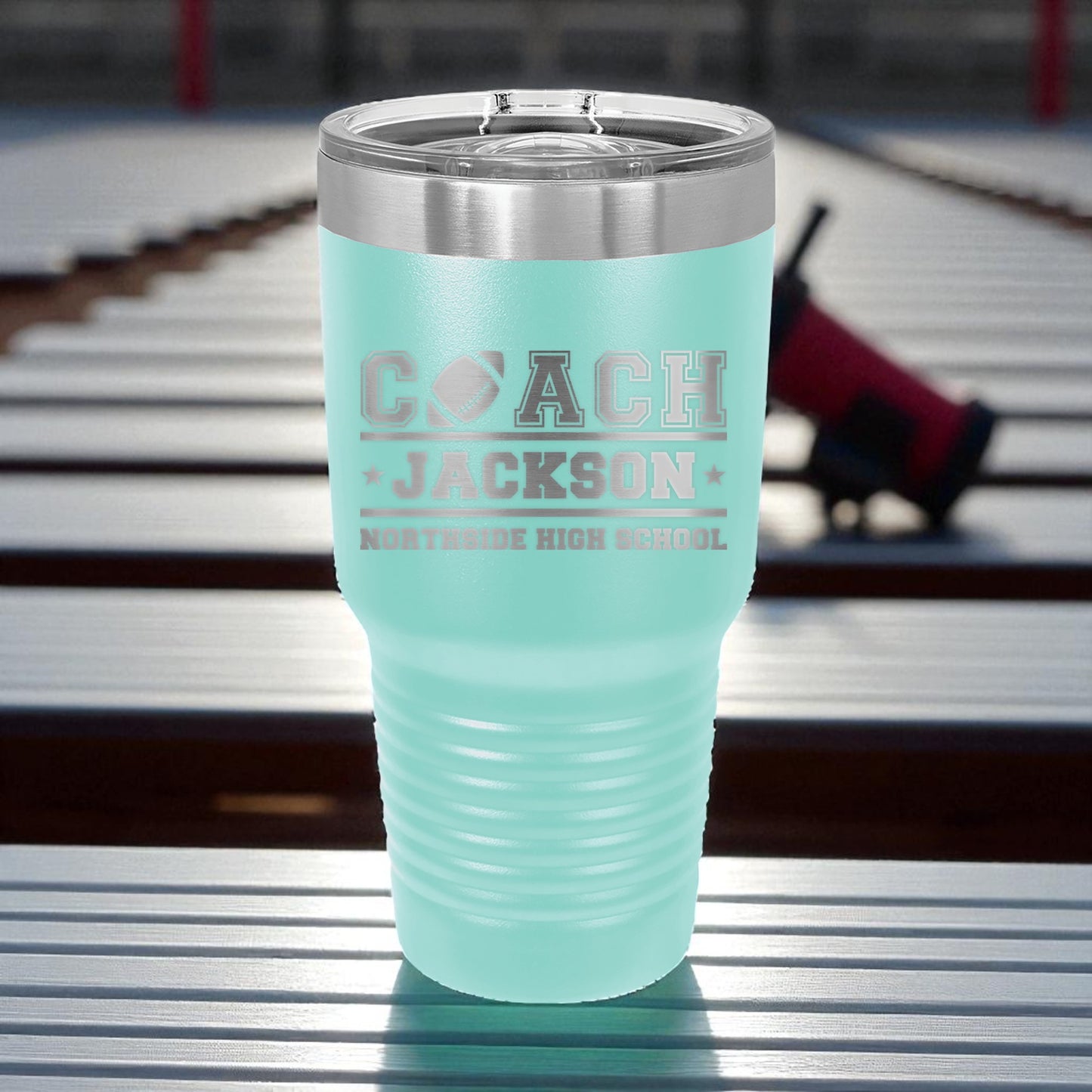 Turquoise tumbler with 'Coach Jackson' text on a metal surface