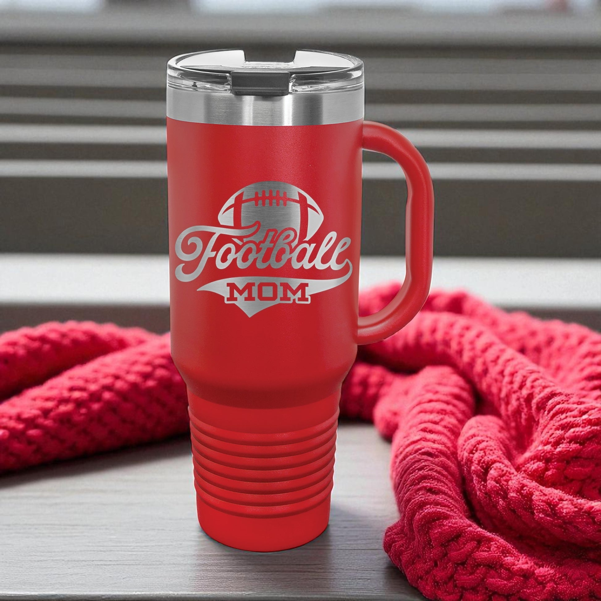 Red travel mug with 'Football Mom' text on a wooden surface with red fabric in the background