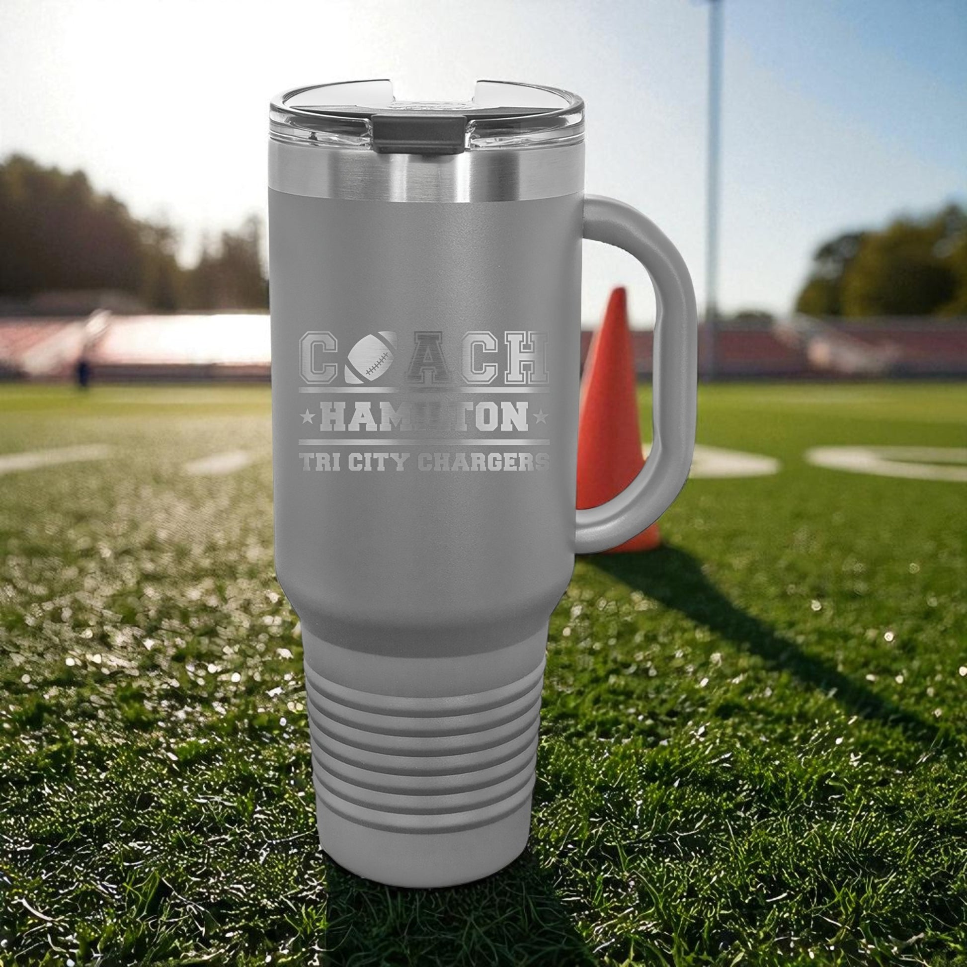 Gray travel mug with engraved text on a grassy field