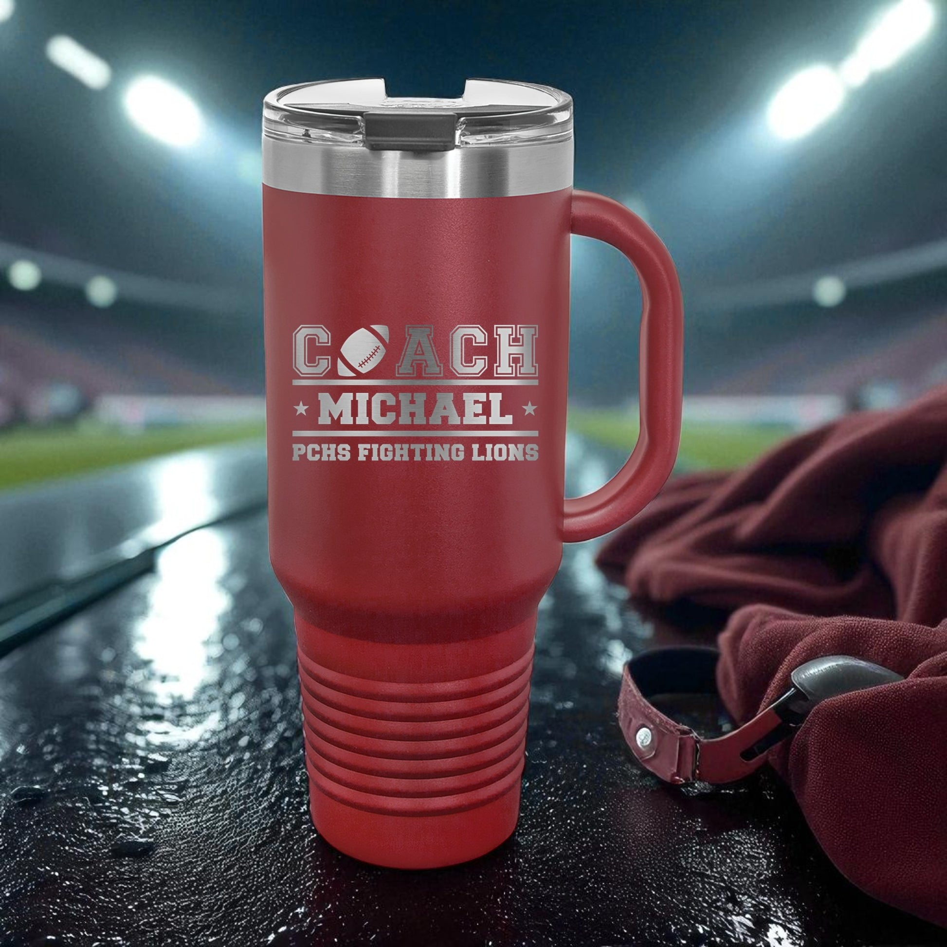 Red travel mug with engraved text on a sports field background