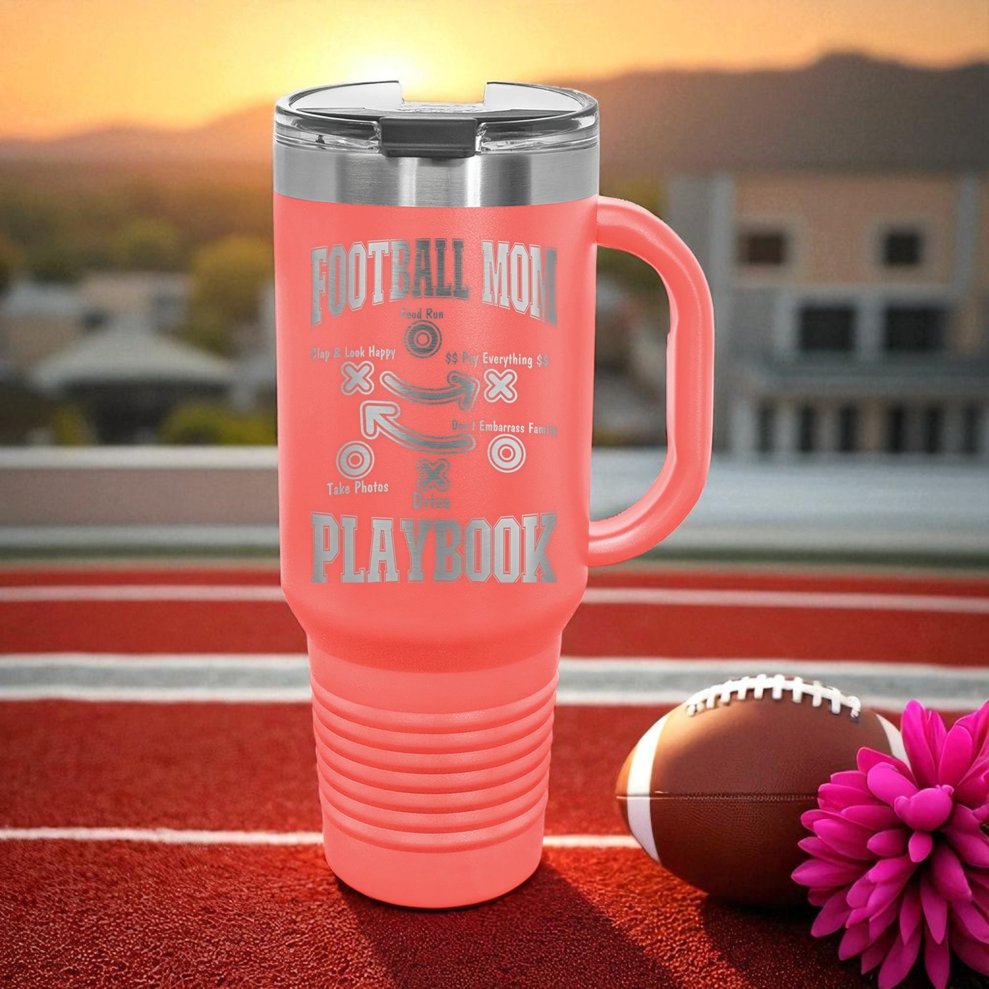 Pink travel mug with 'Football Mom' text on a football field with a sunset background