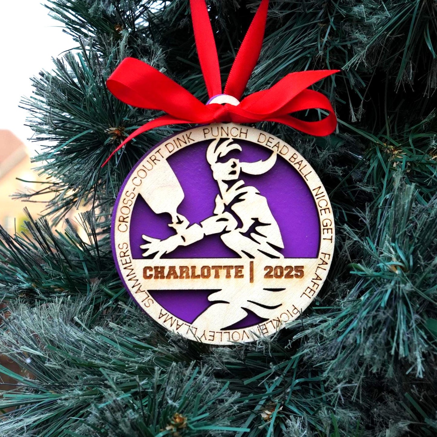 Decorative ornament with a purple circle and white silhouette of a person, tied with a red ribbon on a Christmas tree., Pickleball Ornament