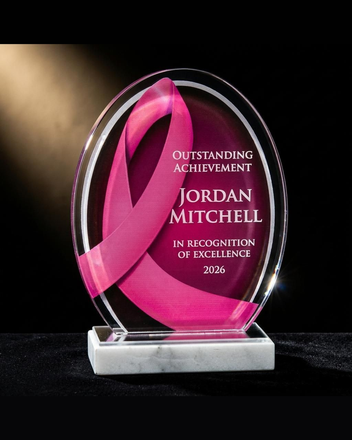 Personalized pink ribbon breast cancer awareness acrylic award on black velvet under a spotlight, engraved survivor recognition keepsake for a Pink October ceremony