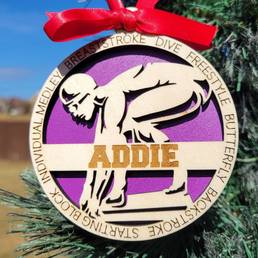 Decorative ornament with swimming-themed design and red ribbon on a Christmas tree.