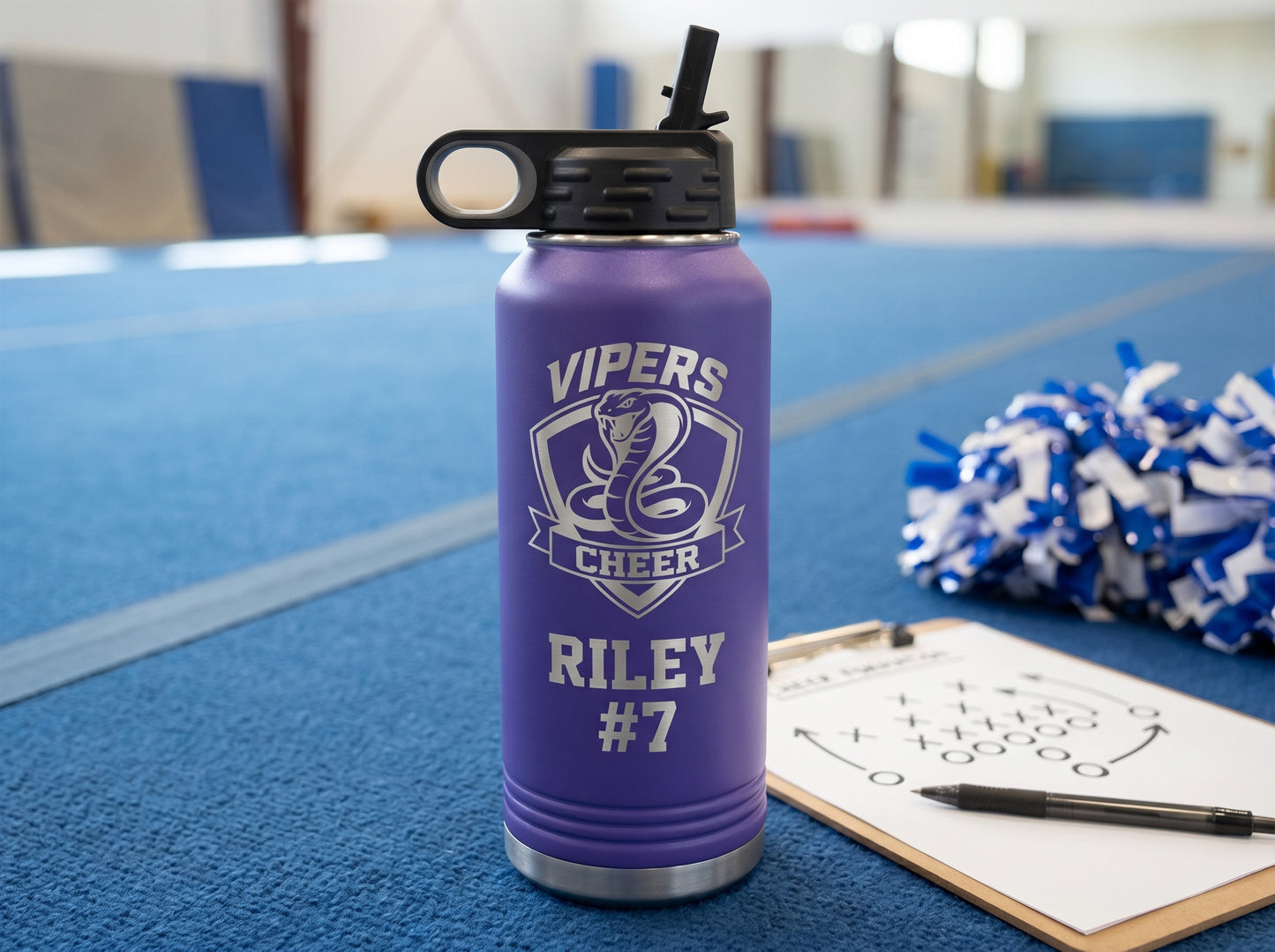 purple engraved cheer water bottle next to coach clipboard on blue gym mat