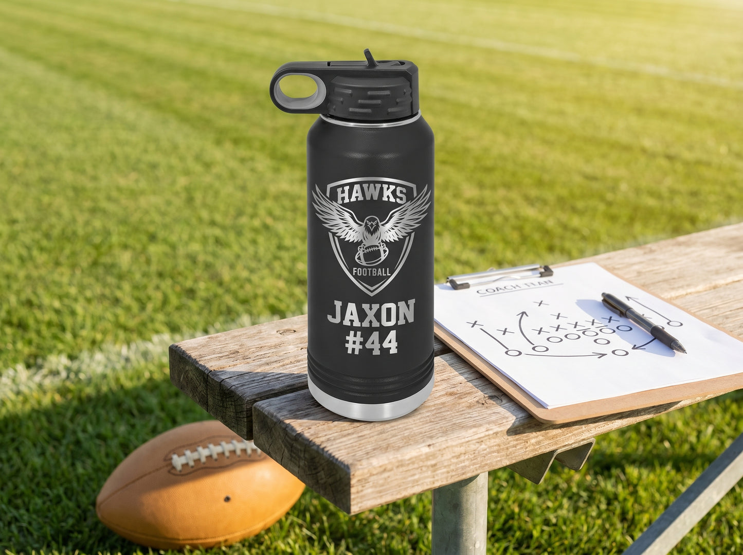 black engraved football water bottle on sideline bench with coach playbook clipboard