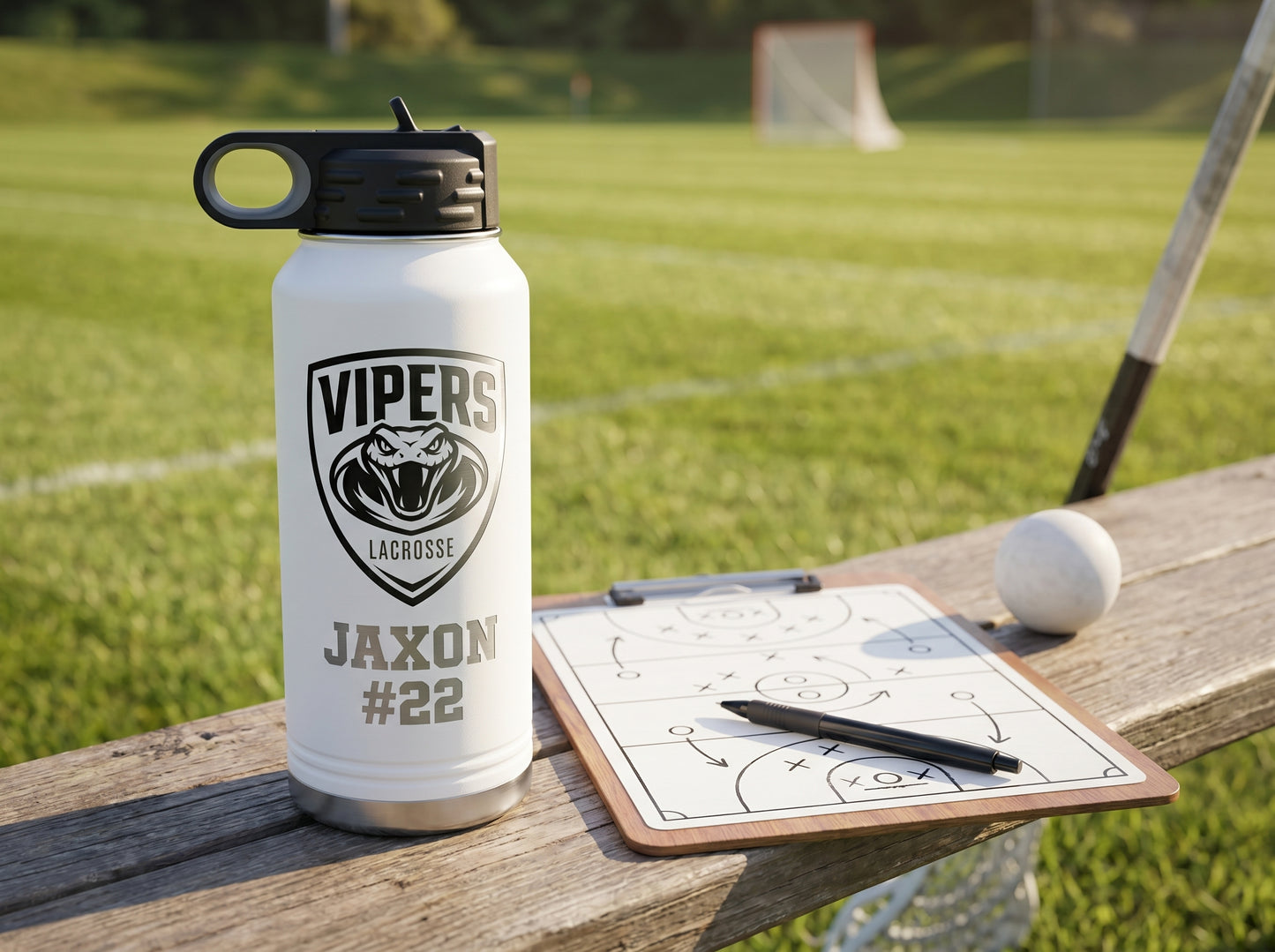 white engraved lacrosse water bottle next to coaches tactics clipboard field background