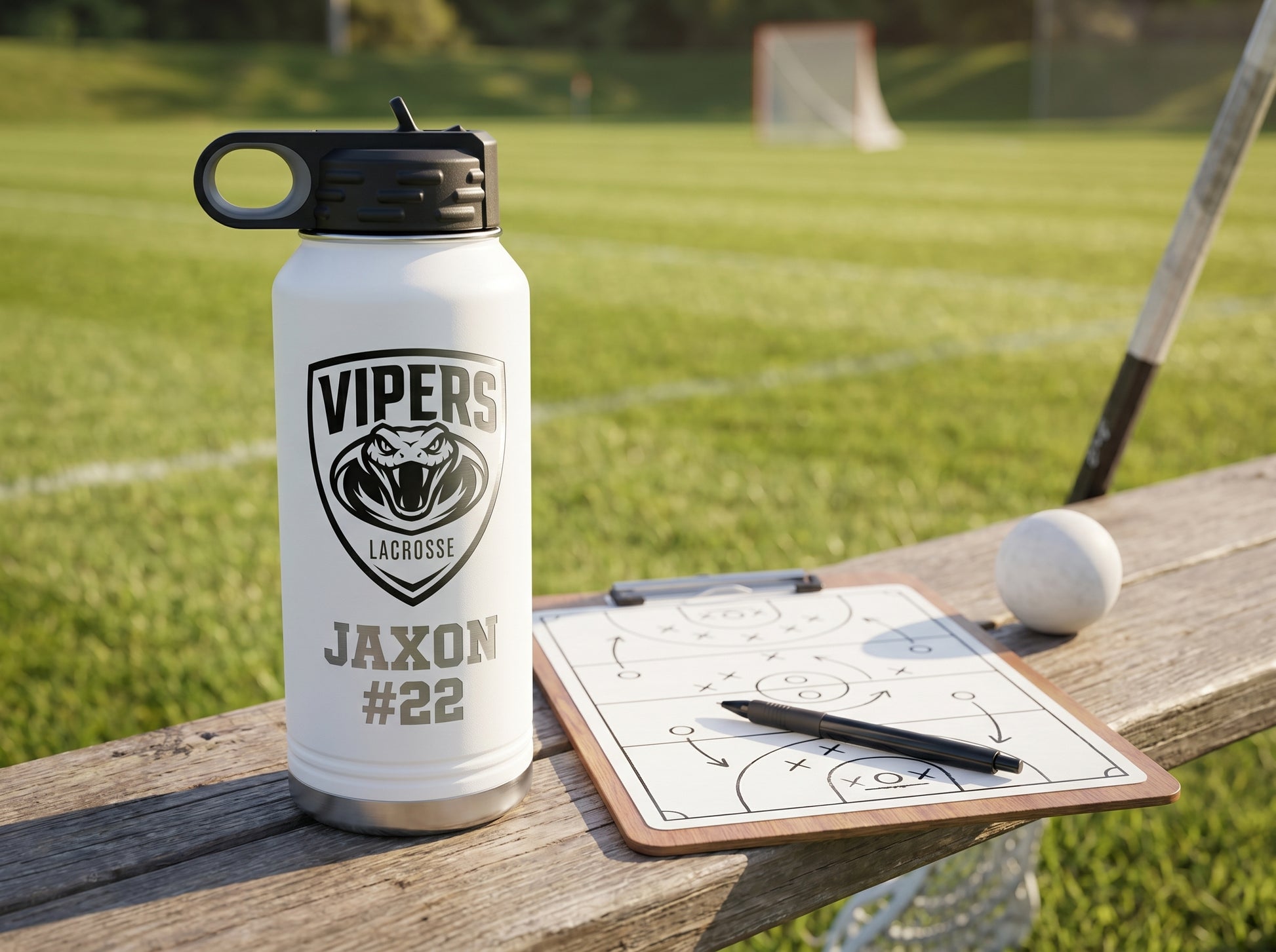 white engraved lacrosse water bottle next to coaches tactics clipboard field background
