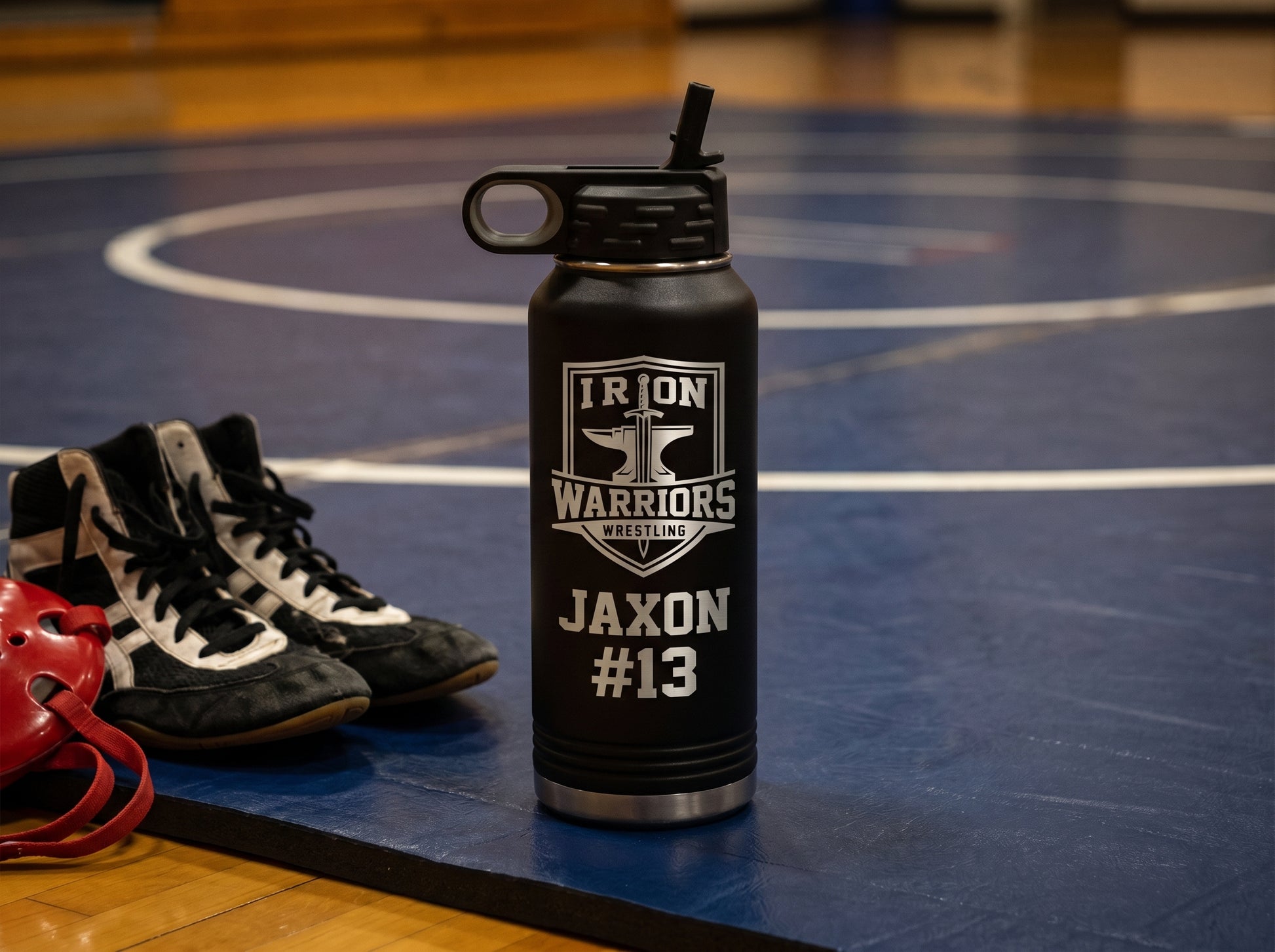 wrestling team water bottle on mat under low gym lights with wrestling shoes and headgear
