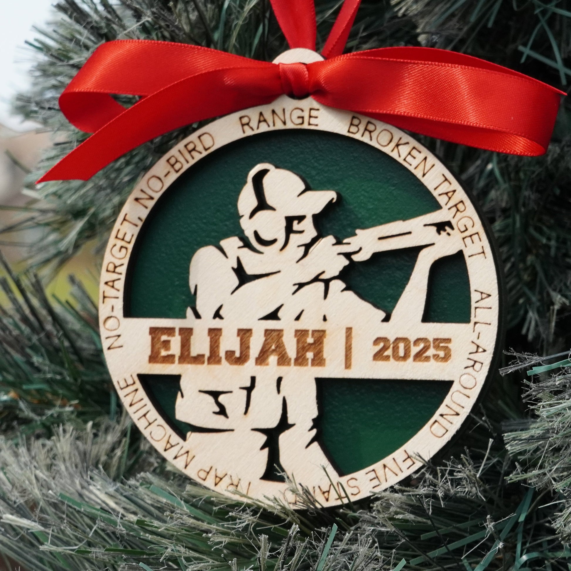 Decorative Christmas ornament with a red ribbon on a tree, featuring the name 'Elijah' and the year '2025'. Decorative Christmas ornament with a silhouette of a person holding a skeet shooting on a christmas tree, Clay Shooting Ornament, Skeet Shooting Gift, Clay Shooter Gift
