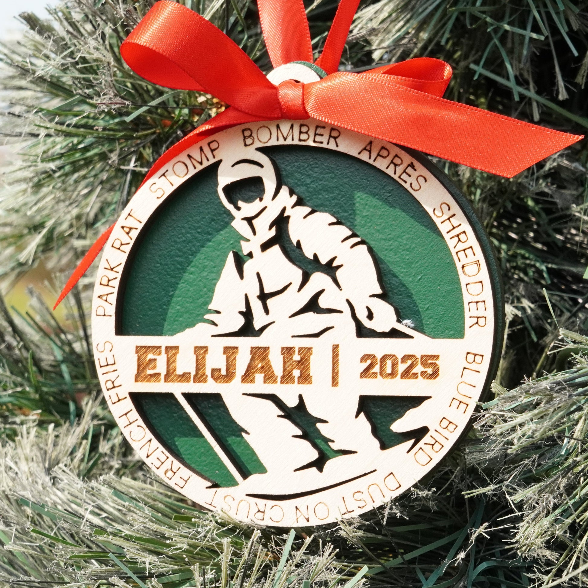 Decorative ornament with a red ribbon on a Christmas tree, featuring the name 'Elijah' and the year '2025'. skier ornament, skiing ornament