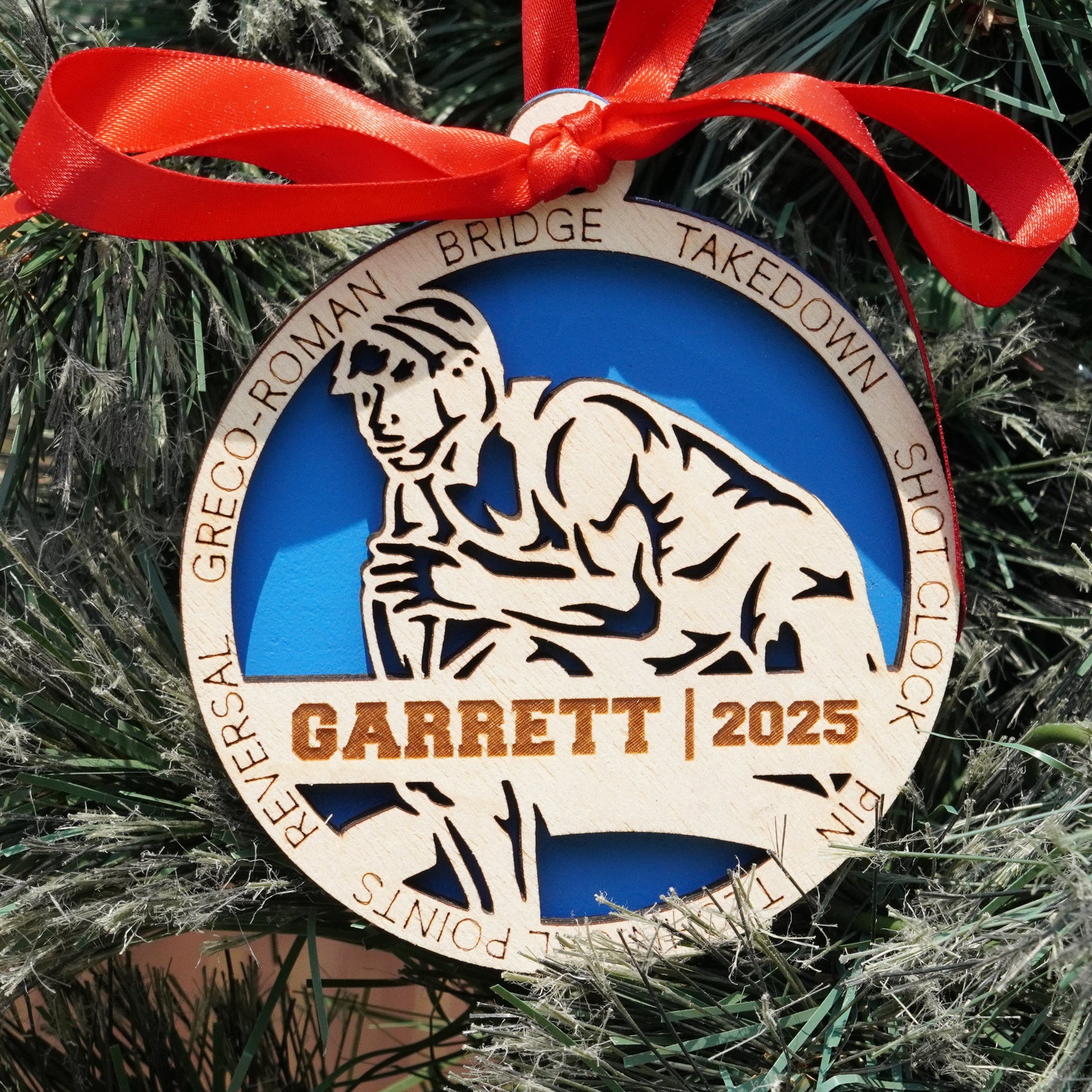 Decorative ornament with a blue center and gold border, featuring a silhouette of a person and text, hanging on a Christmas tree. Decorative ornament with a red ribbon on a Christmas tree, featuring a wrestler, wrestling ornament, christmas gift for wrestler, wrestling ornament,