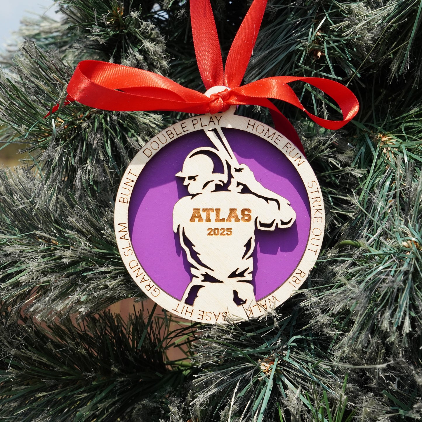 Decorative ornament with a purple circle and white silhouette, tied with a red ribbon on a Christmas tree.