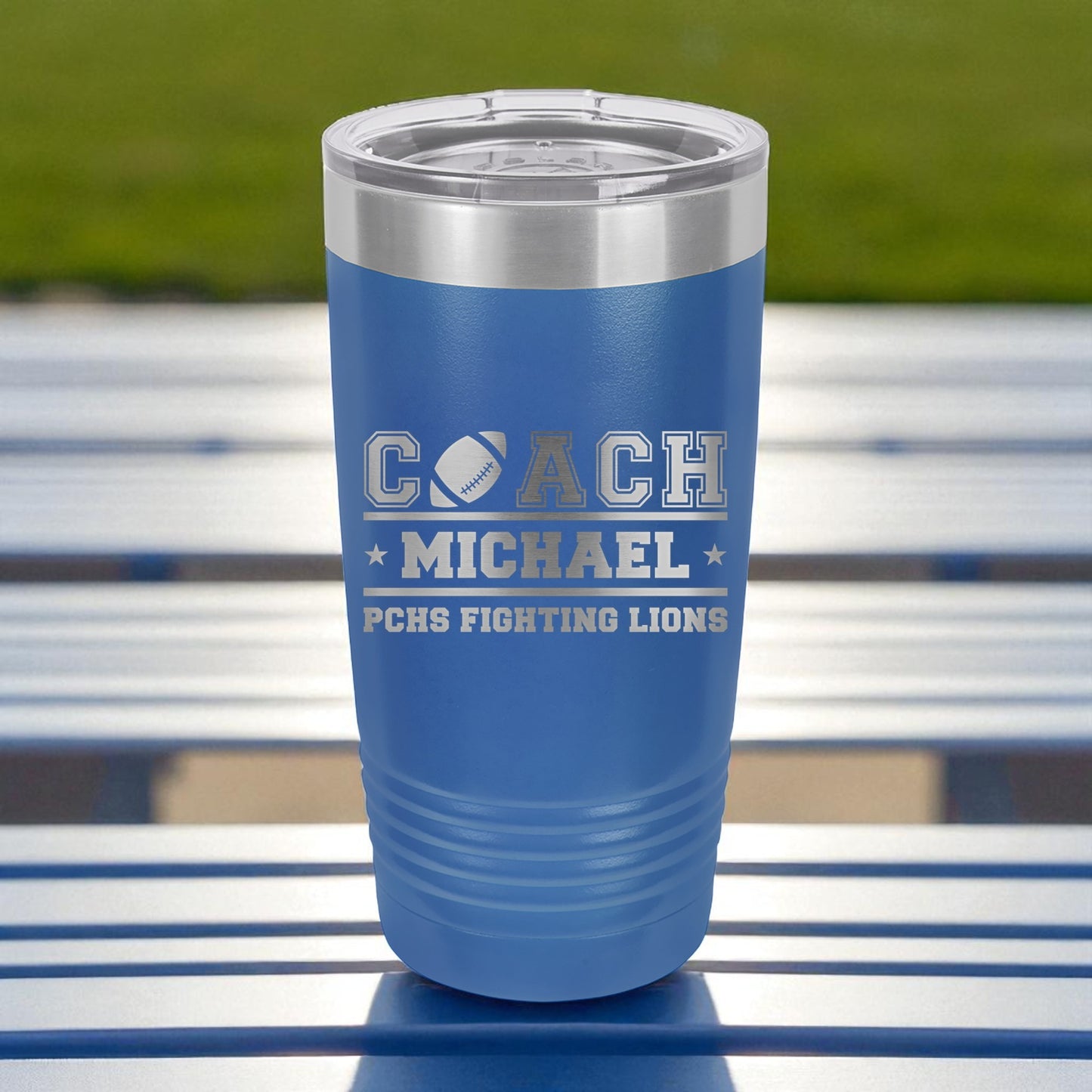 Blue tumbler with 'COACH MICHAEL' and 'PCHS FIGHTING LIONS' text on a metal surface.