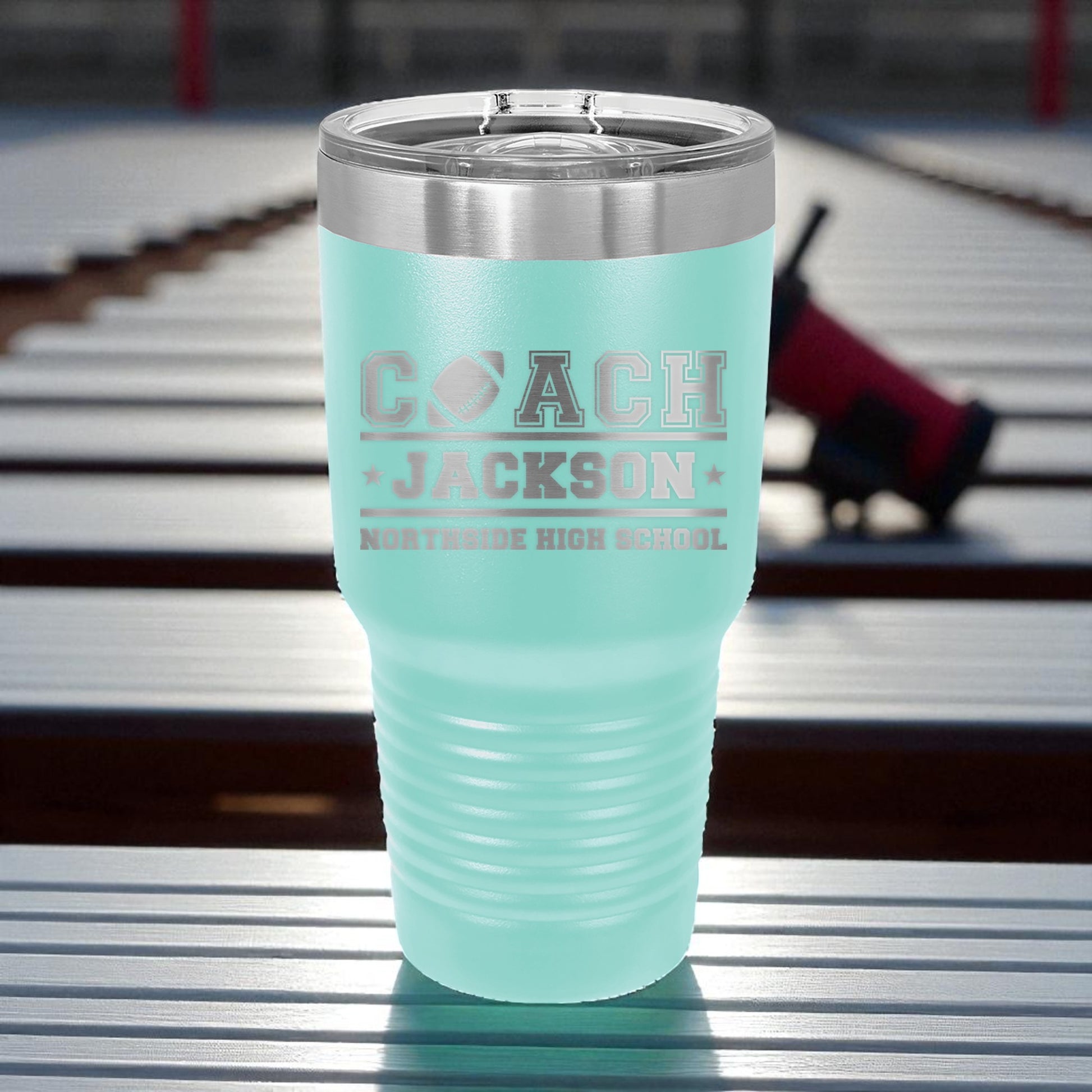 Turquoise tumbler with 'Coach Jackson' text on a metal surface