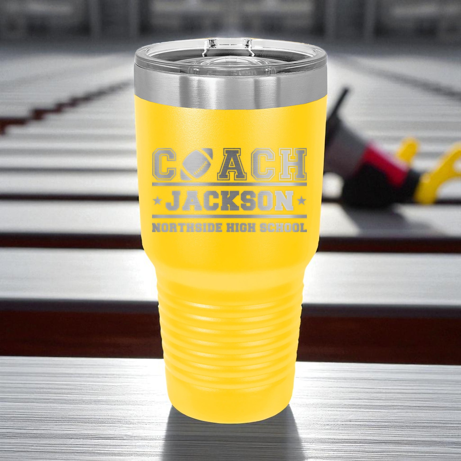 Yellow tumbler with 'Coach Jackson Northside High School' text on a blurred background