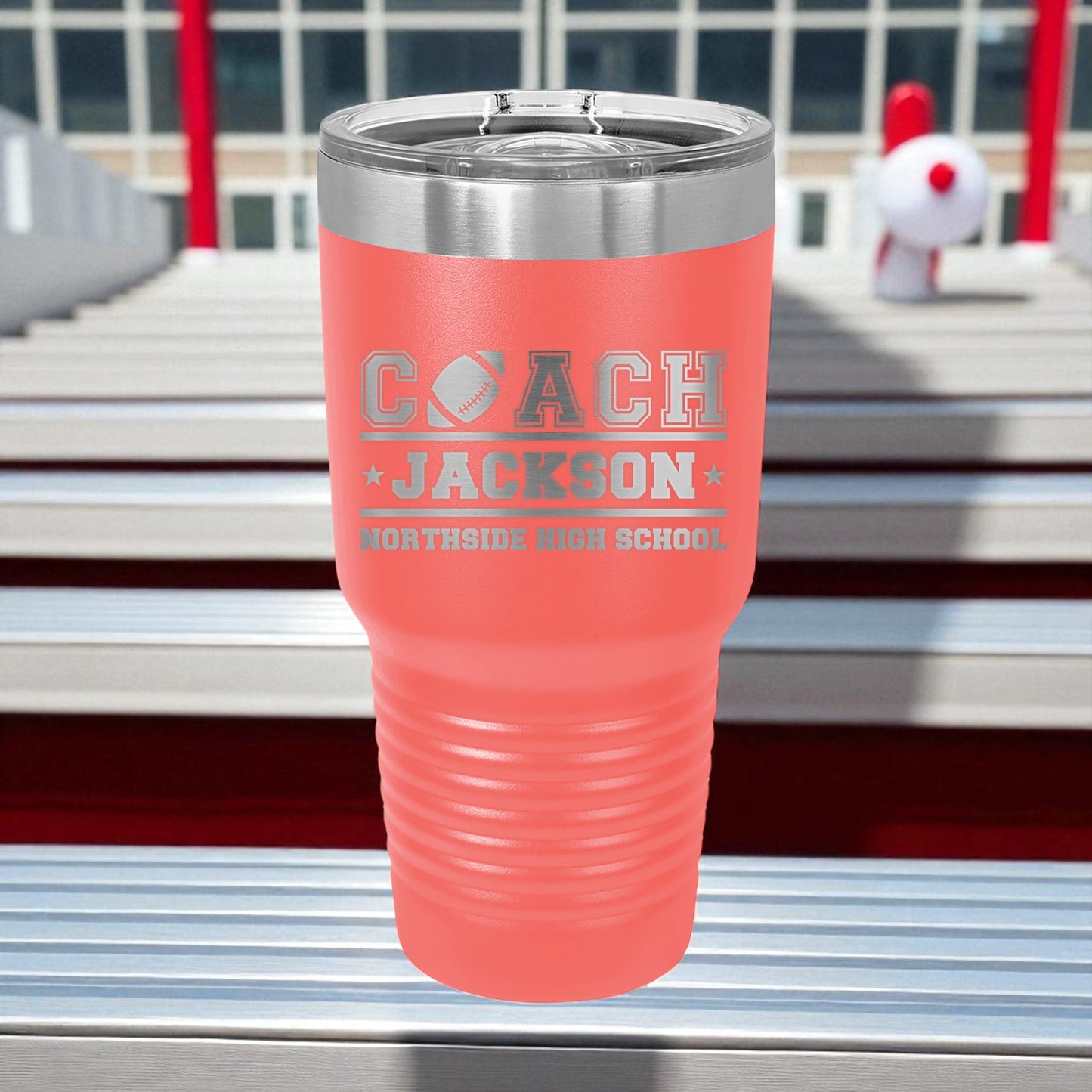 Pink tumbler with 'Coach Jackson' engraving on a metal surface