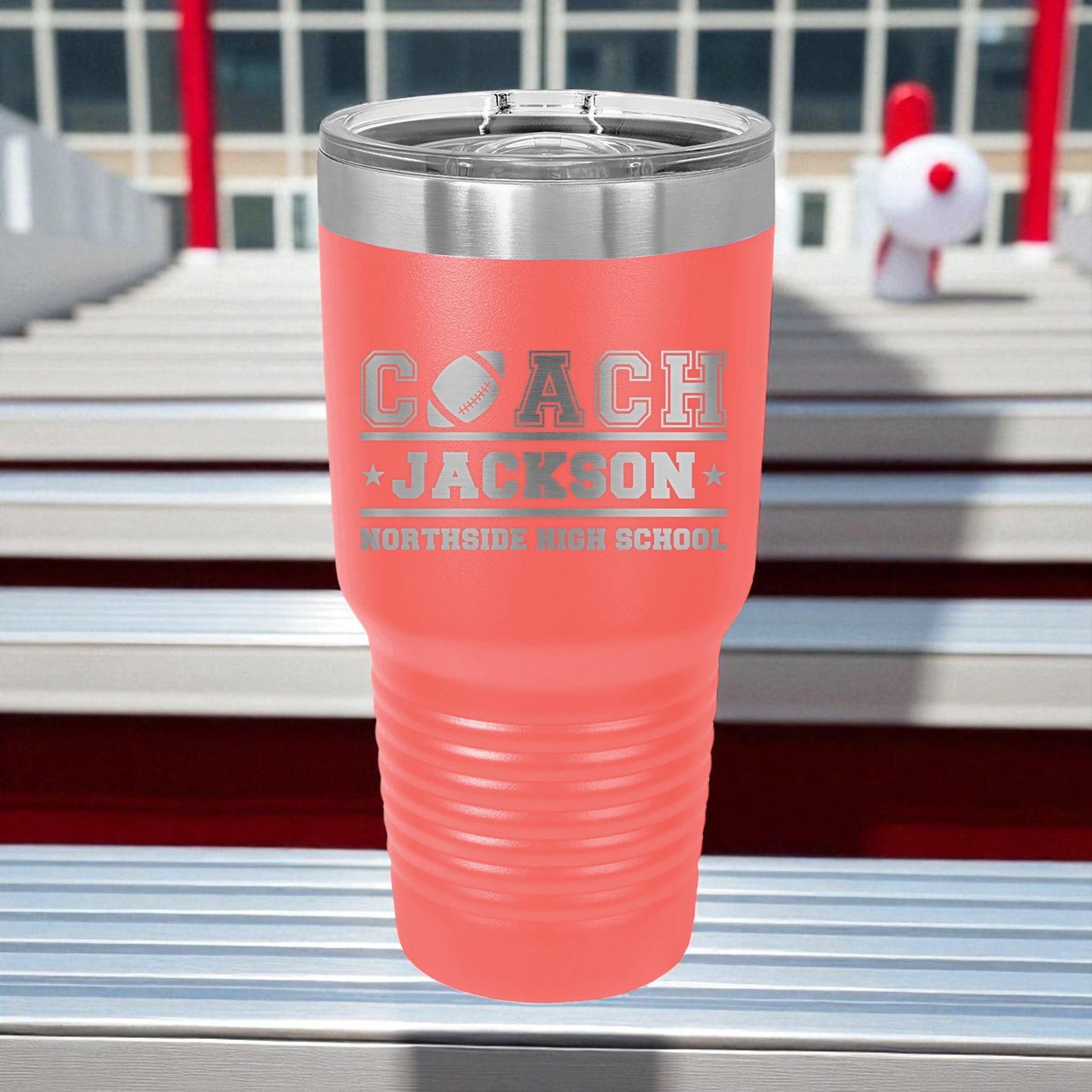 Pink tumbler with 'Coach Jackson' engraving on a metal surface