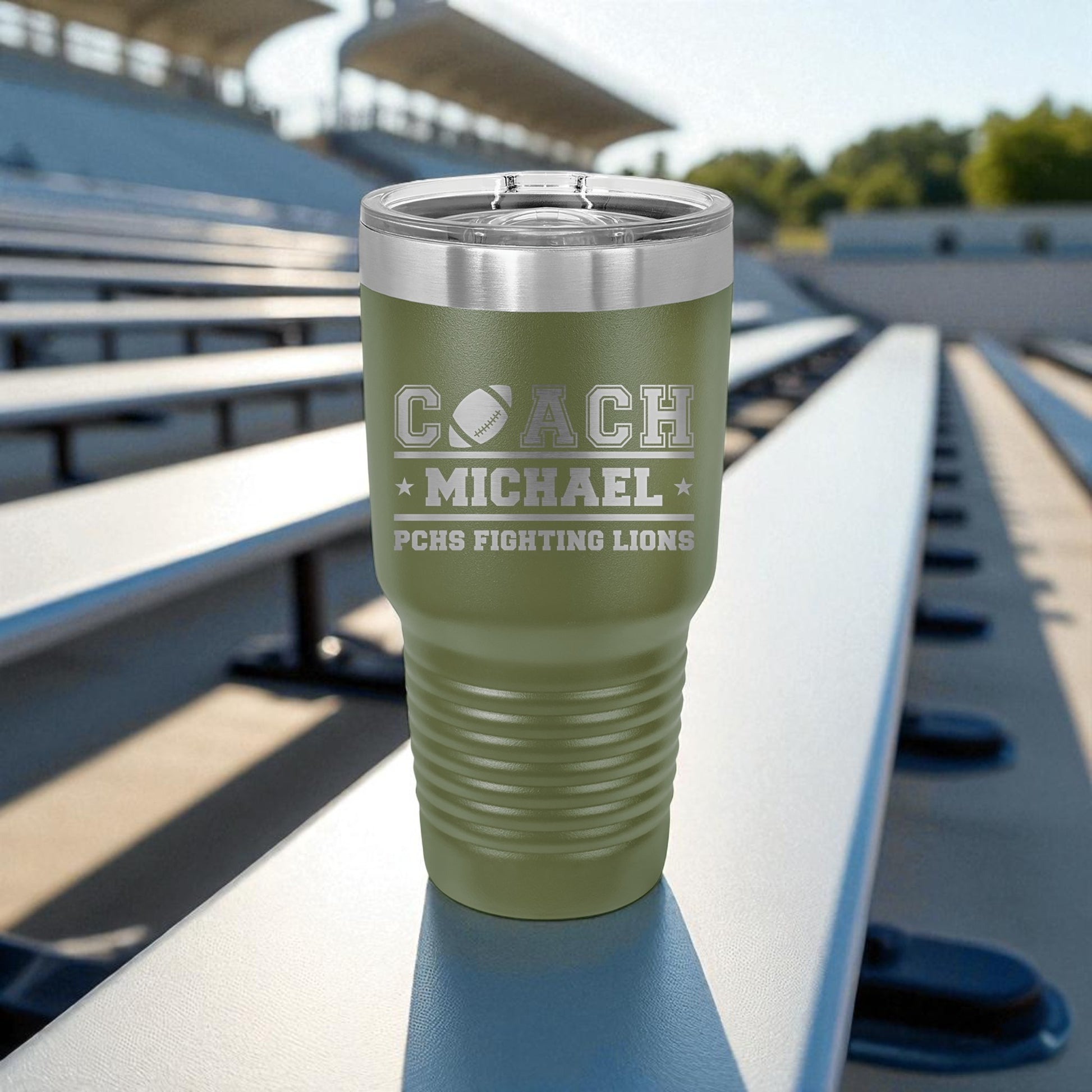 Green tumbler with 'Coach Michael' engraving on a stadium bench
