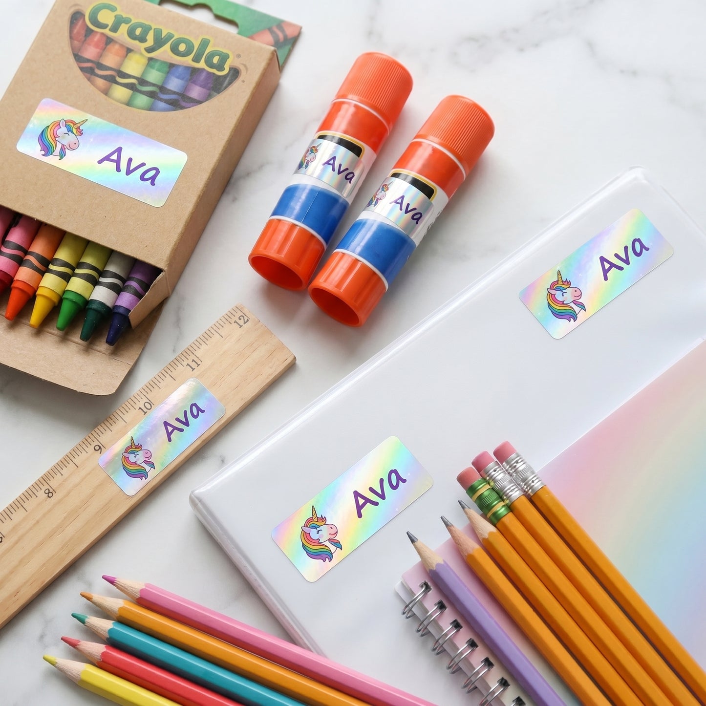 Unicorn name labels on a crayon box, glue sticks, ruler and pencils