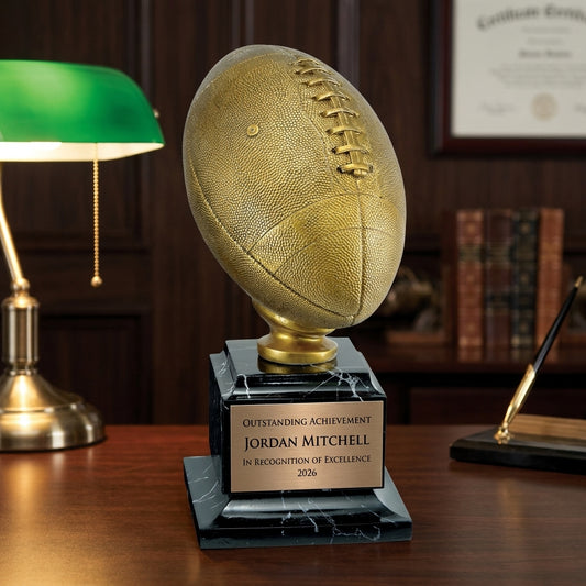 Personalized Antique Gold Football Resin Trophy resin award on a warm executive desk with a green banker's lamp, engraved corporate recognition and retirement gift