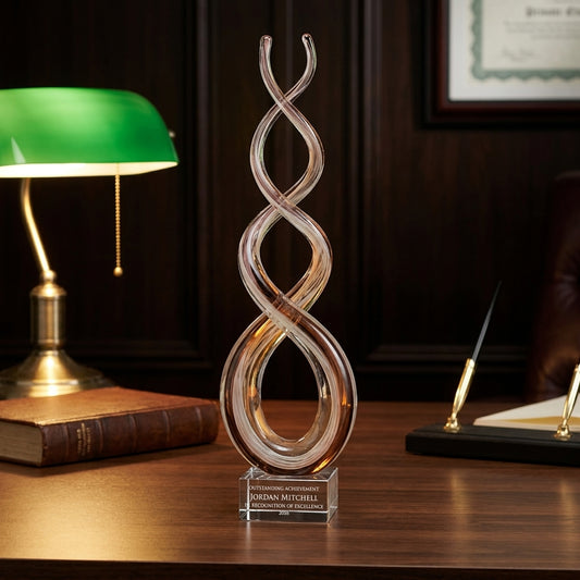 Personalized Amber Caramel Infinity art glass award on a warm executive desk with a green banker's lamp, engraved corporate recognition and retirement gift