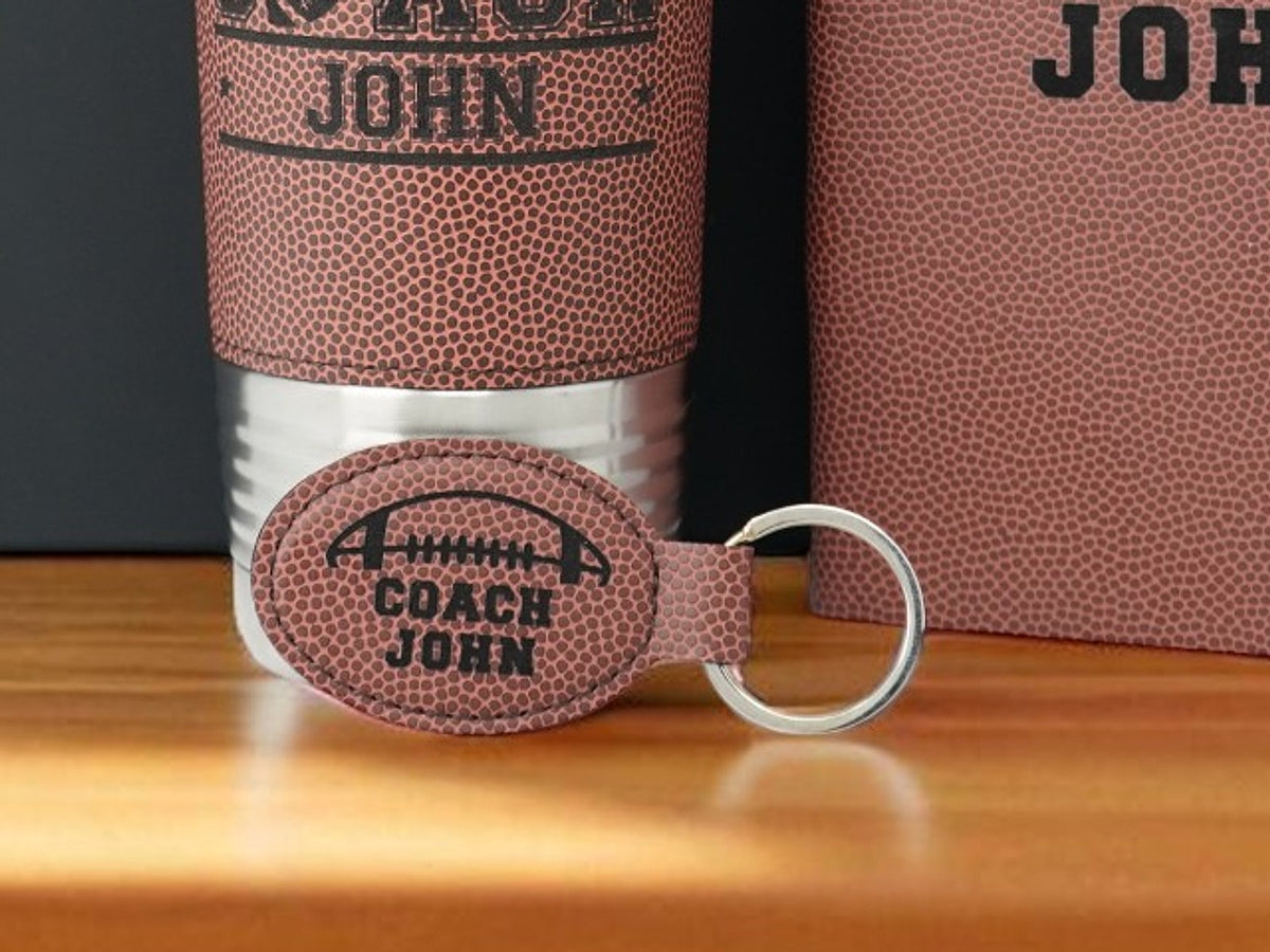 Personalized football coach keychain, football leatherette oval engraved with a football, COACH and the name John, leaning on the matching coach tumbler