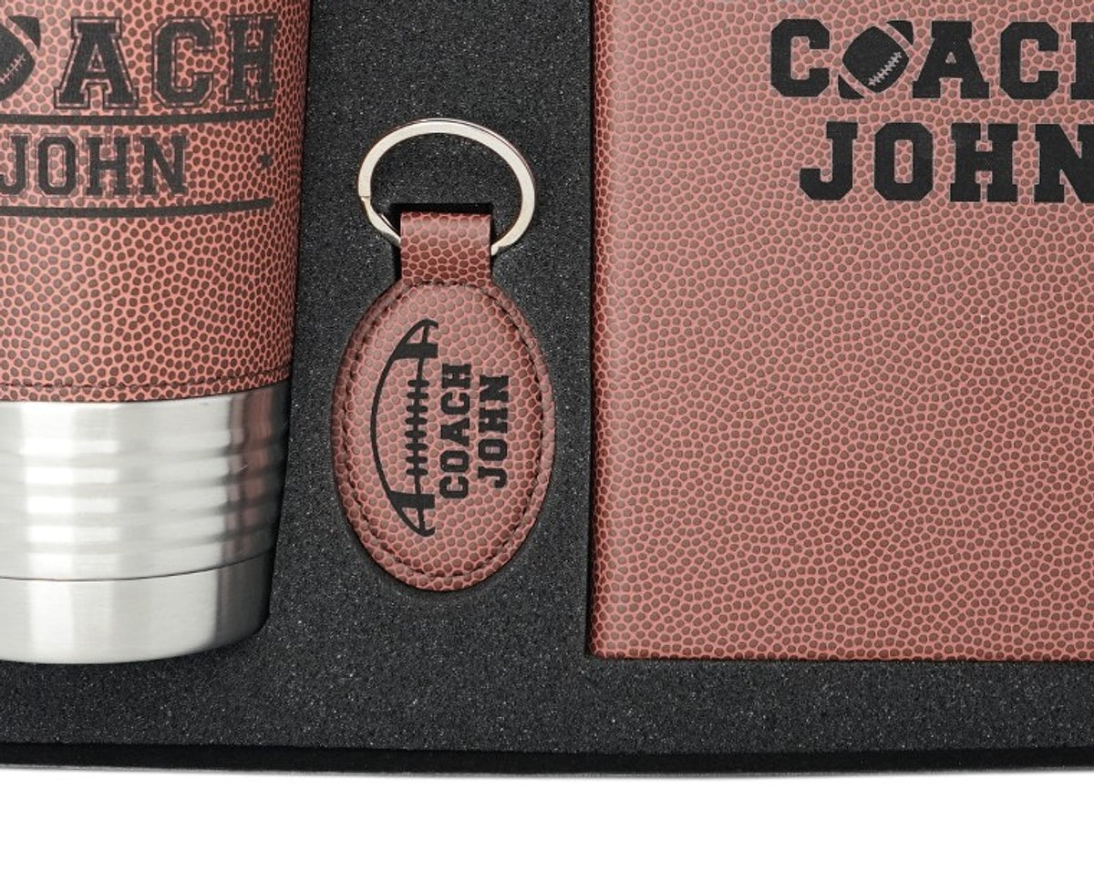 Engraved football leather coach keychain with silver split ring, between the engraved tumbler and journal in the gift box