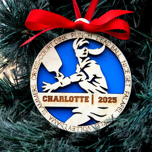 Decorative ornament with a red ribbon on a Christmas tree, featuring text and a logo.